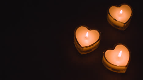 Three-Romantic-Lit-Heart-Shaped-White-Candles-On-Black-Background-Being-Blown-Out